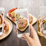 Three iPhones held up by different hands taking picture of food on table