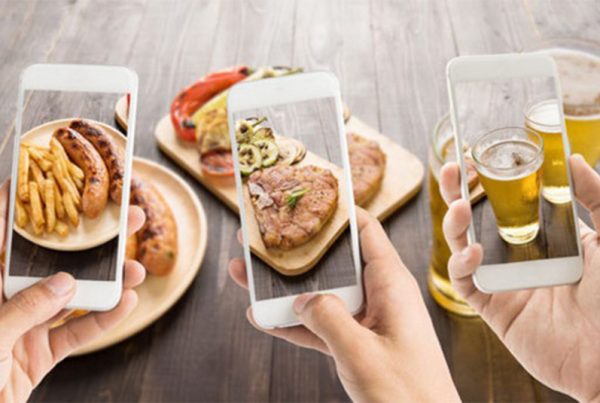 Three iPhones held up by different hands taking picture of food on table