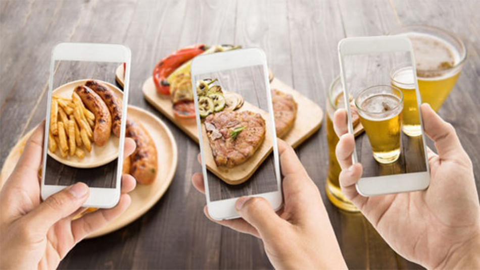 Three iPhones held up by different hands taking picture of food on table