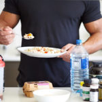 Athlete eating bowl of oatmeal with eggs, supplements and protein powder in front of him