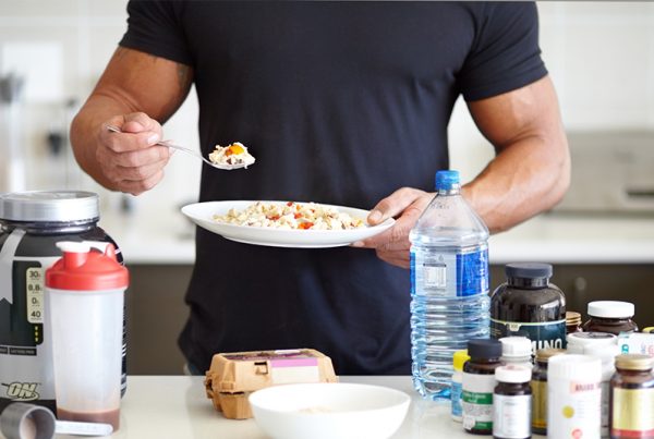 Athlete eating bowl of oatmeal with eggs, supplements and protein powder in front of him