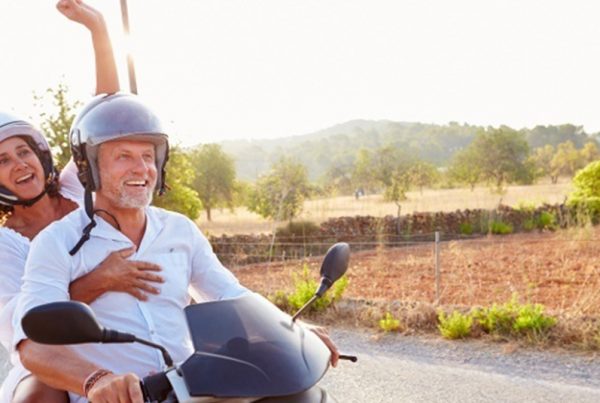 Smiling older couple on motorcycle with woman's arm raised