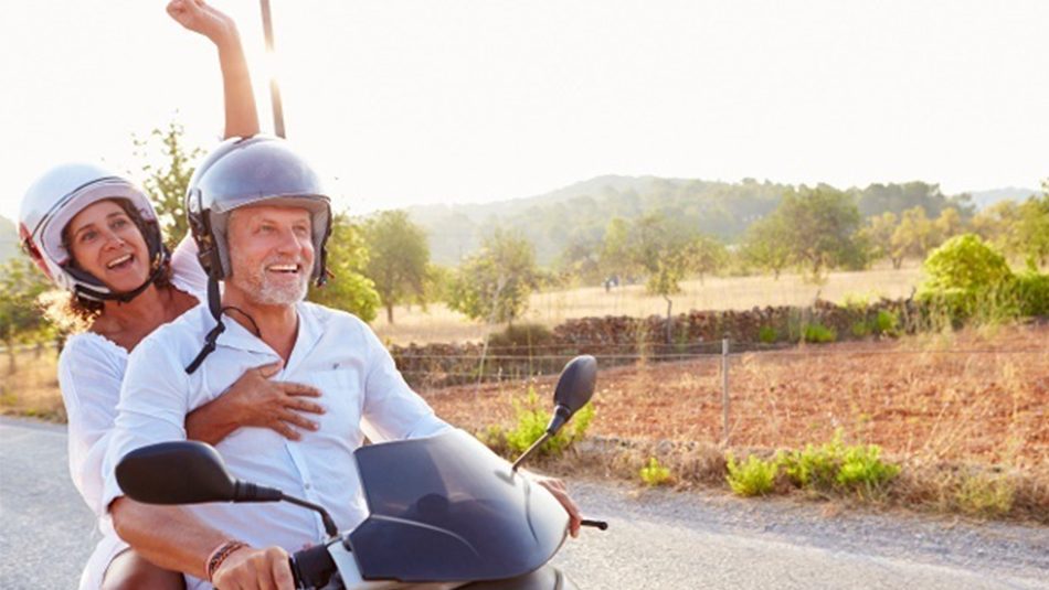 Smiling older couple on motorcycle with woman's arm raised