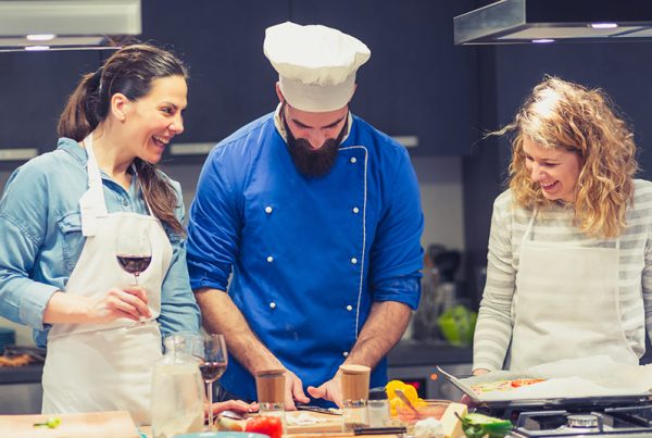 Chef in blue coat instructing two women students on prepping food