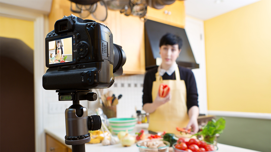Women food blogger standing in kitchen behind camera with fresh produce