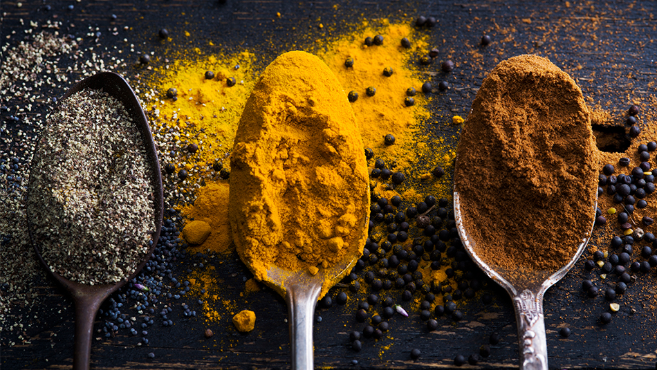 three spoons on black background containing ground turmeric, pepper, and cinnamon