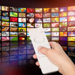 Hand with tv remote in front of grid of televisions