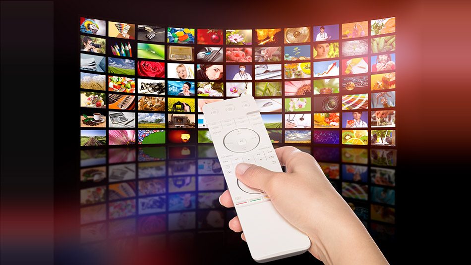 Hand with tv remote in front of grid of televisions
