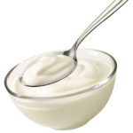 Spoonful of plain yogurt from glass bowl on white background