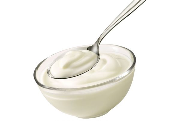 Spoonful of plain yogurt from glass bowl on white background
