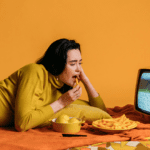 A woman relaxes on a bed with a TV and a bowl of chips, highlighting CPG and food branding in marketing.