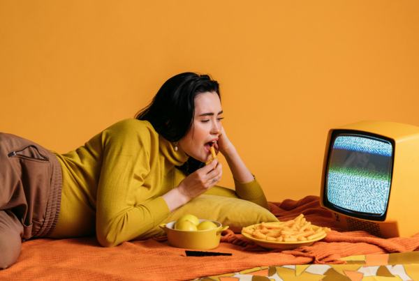 A woman relaxes on a bed with a TV and a bowl of chips, highlighting CPG and food branding in marketing.